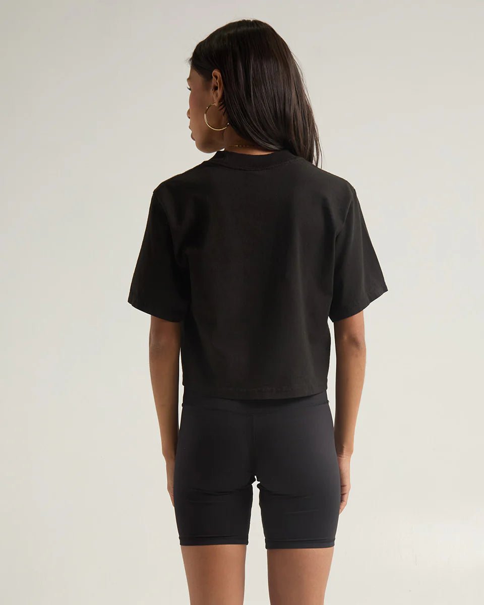 Back view of a woman wearing a black garment dye crop top and cycling shorts, showcasing a modern, stylish look.