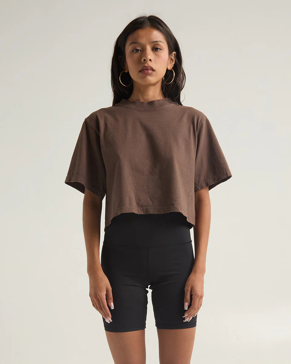 Model wearing a brown garment dye crop top with a modern fit, paired with black bike shorts, showcasing contemporary style.