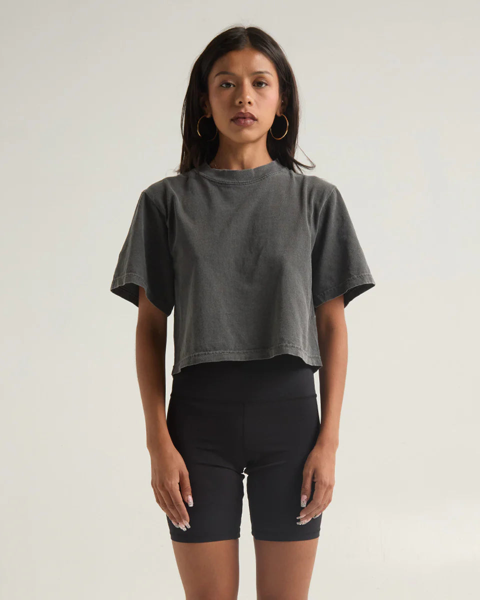 Woman wearing a GARMENT DYE CROP TOP in charcoal gray paired with black shorts, showcasing a modern and stylish look.