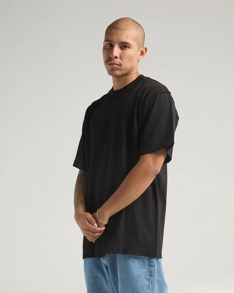 Model wearing the SHAKA WEAR GARMENT DYE REVERSE TEE in black, showcasing its heavyweight fabric and unique inside-out design.