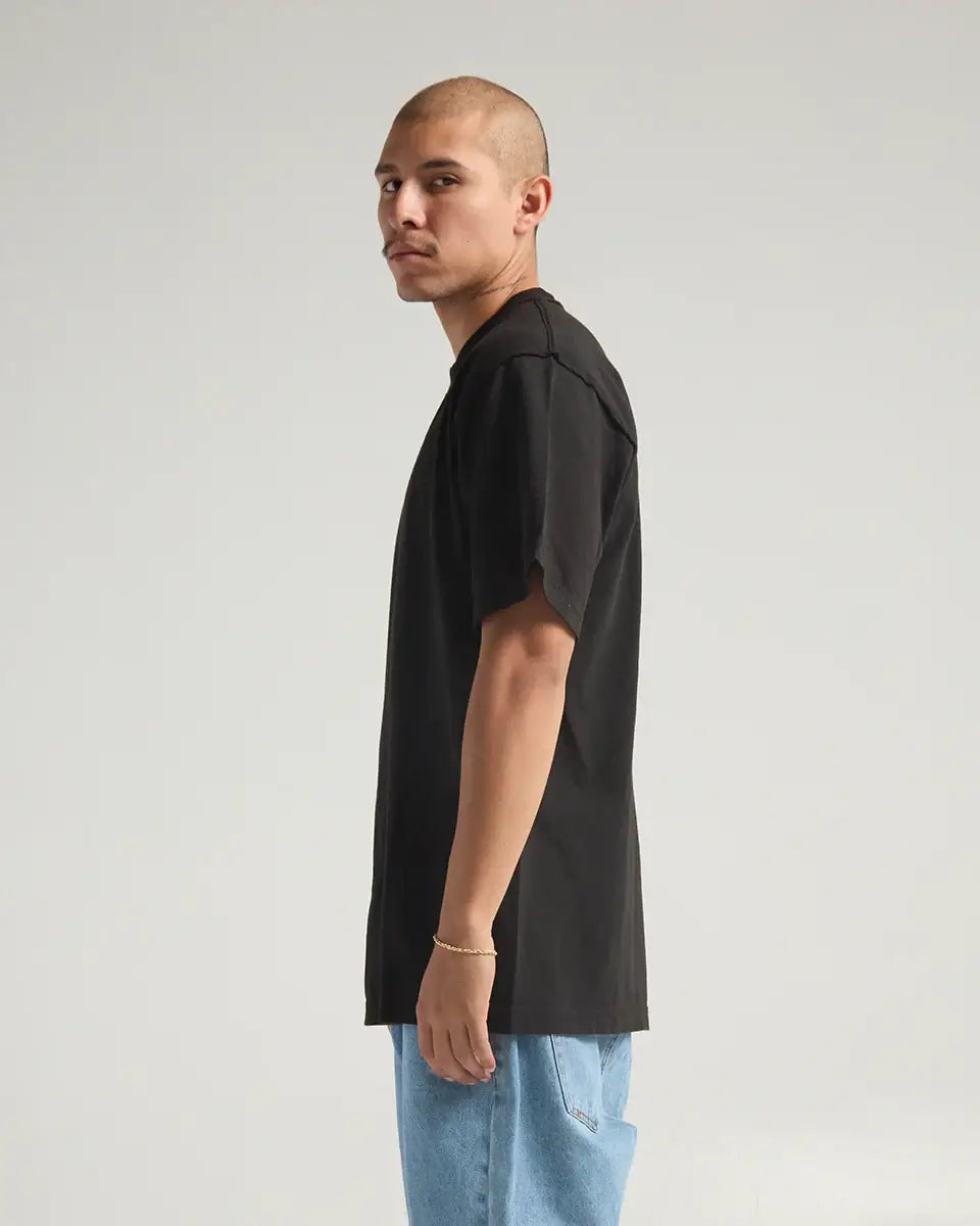 Model wearing the SHAKA WEAR GARMENT DYE REVERSE TEE in black, showcasing its unique inside-out design and heavyweight fabric.